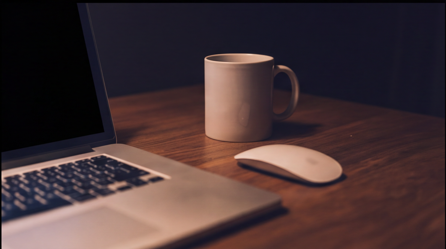 Close-up of a laptop, mug and mouse on a warm wooden desk