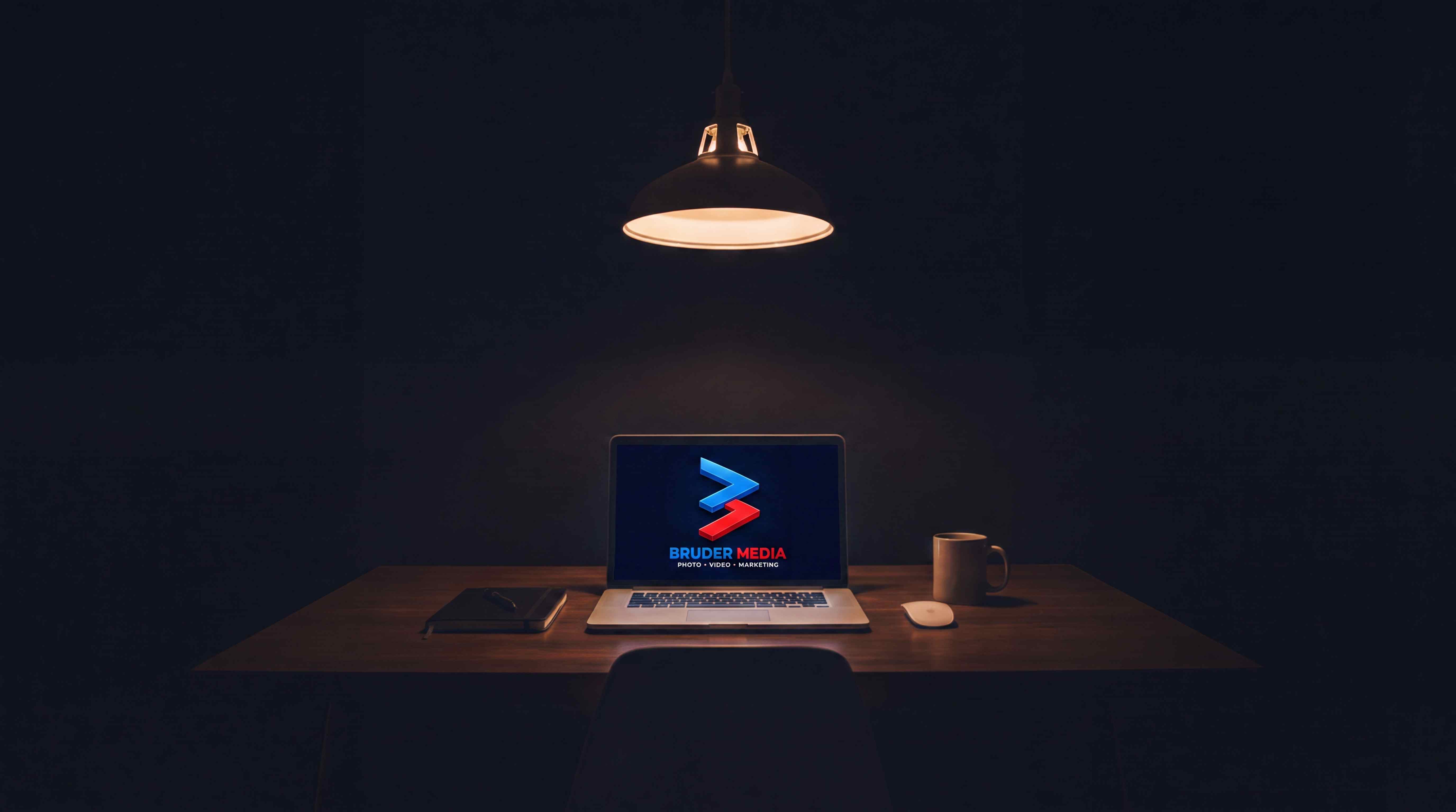 Laptop on a desk under a hanging lamp showing the Bruder Media logo