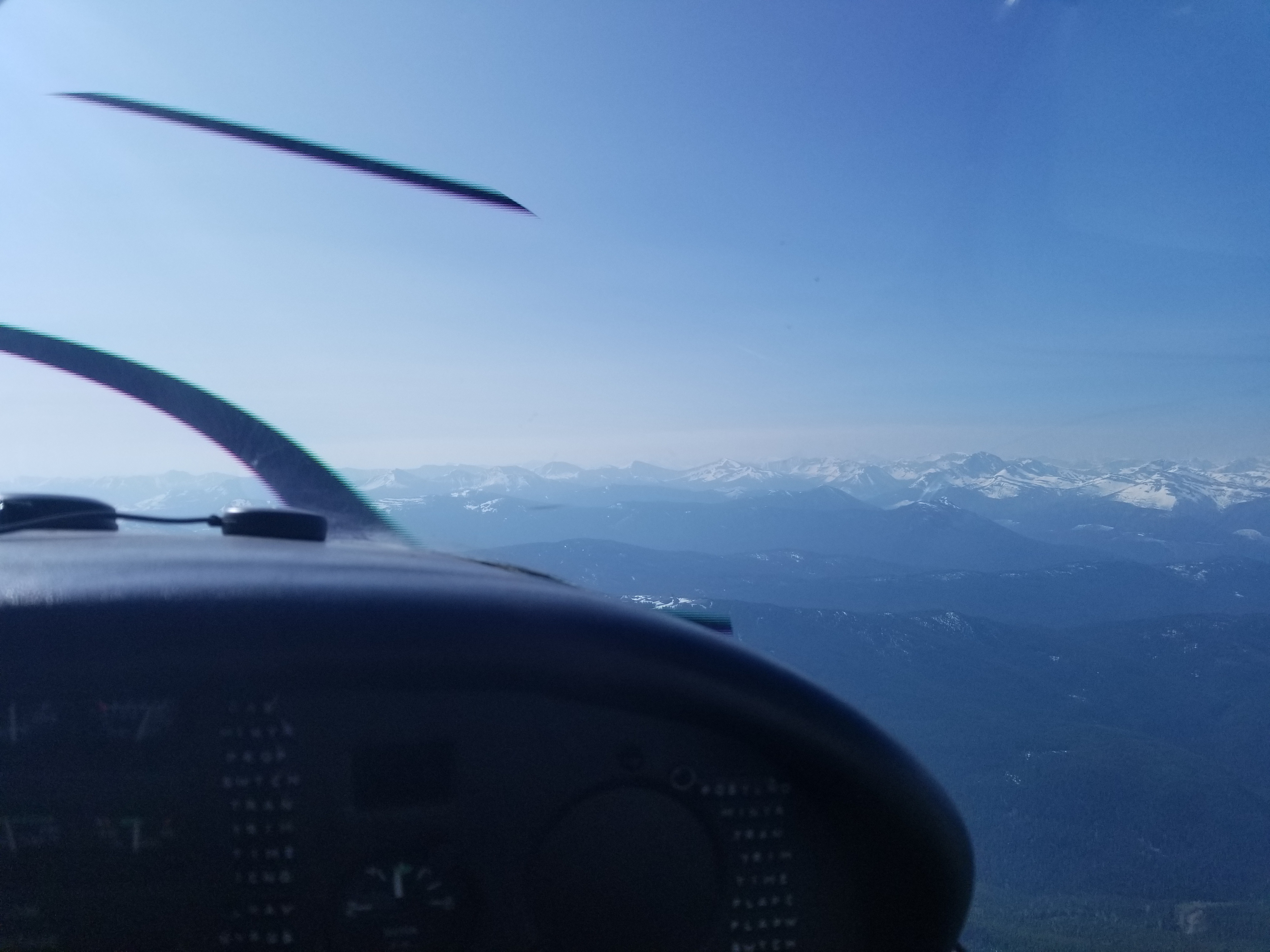 View from a small aircraft cockpit toward snow-capped mountains