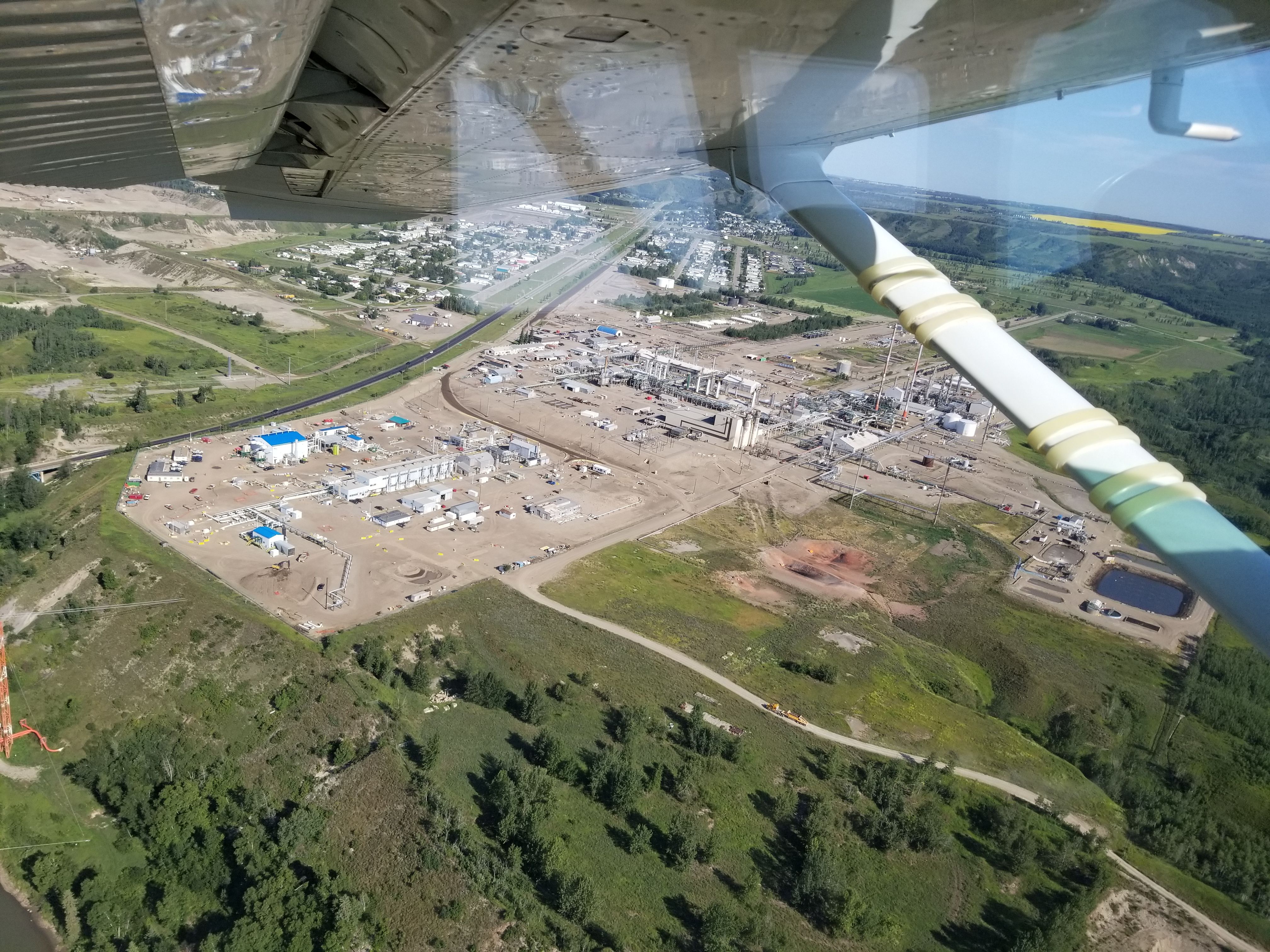 Aerial view from under an aircraft wing of an industrial plant beside a town and river