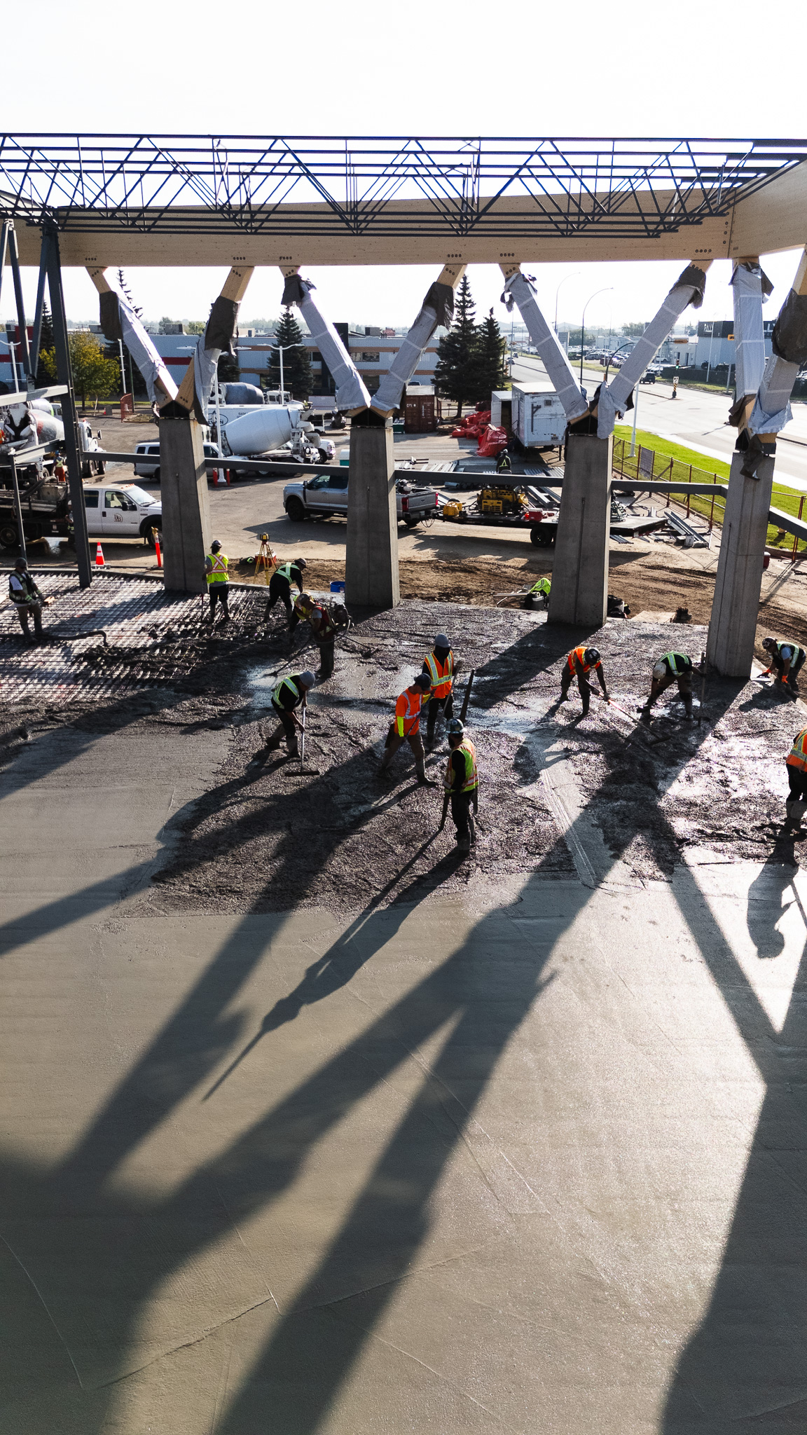 Workers in safety vests pouring concrete under structural canopy