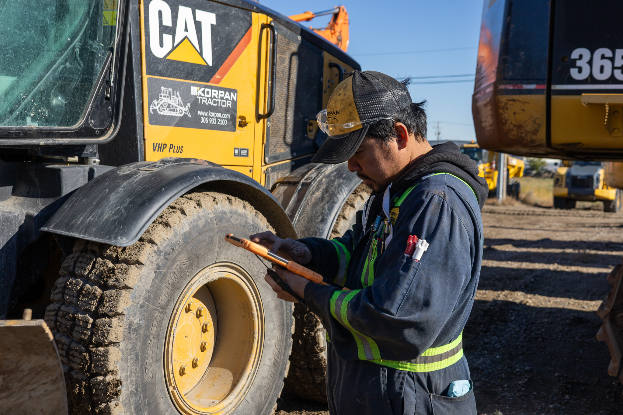 Korpan Tractor technician checking a tablet beside a CAT grader