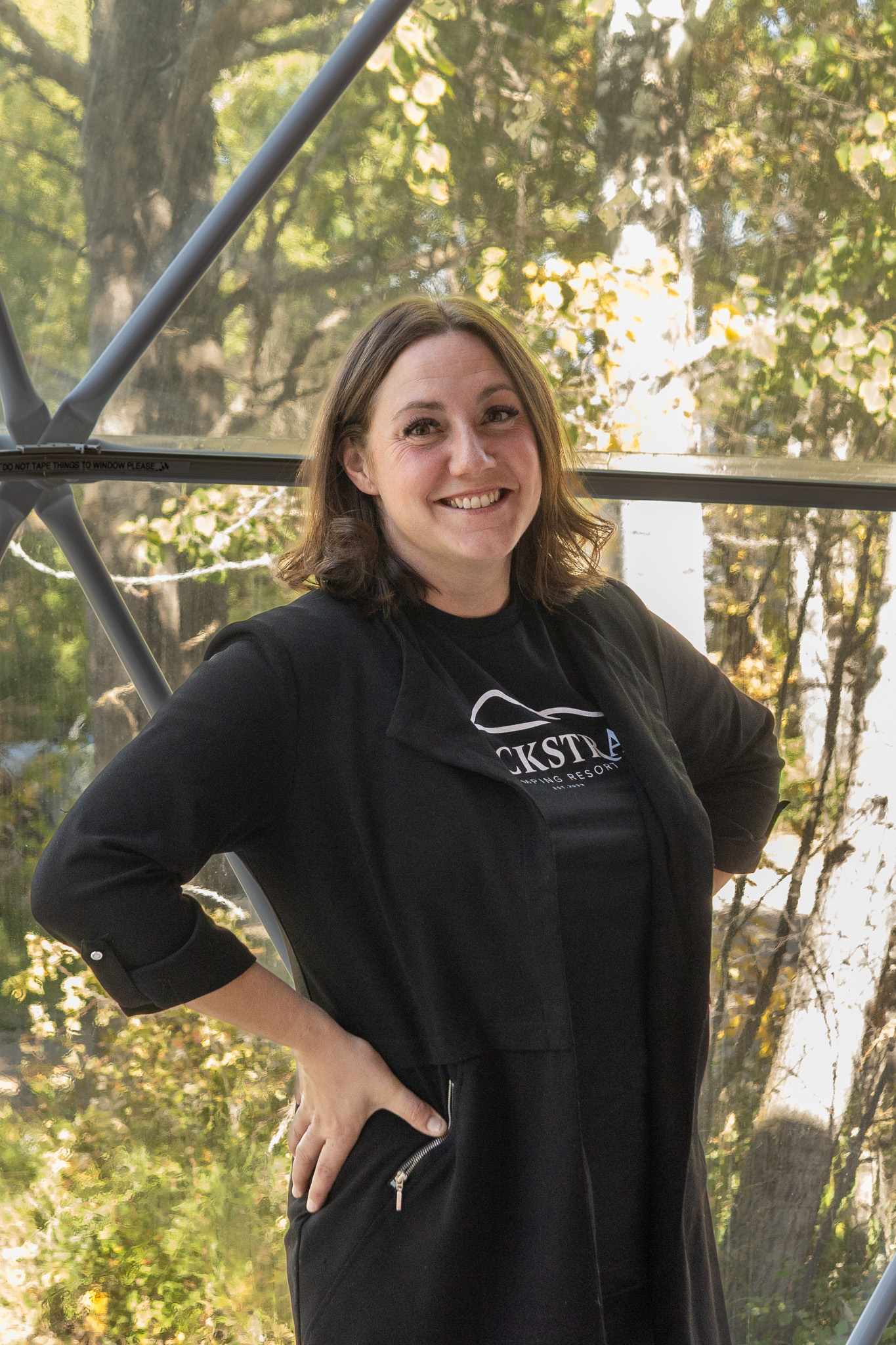 Smiling woman in a black Blackstrap Glamping Resort tee inside a geodesic dome